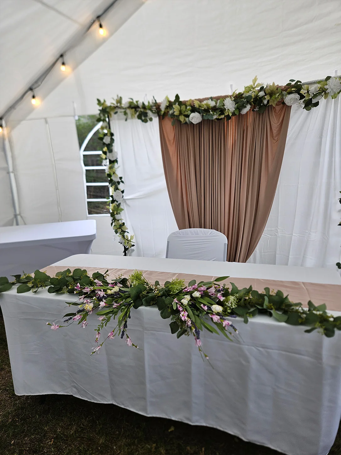 Floral event backdrop and decorated head table inside a lit tent