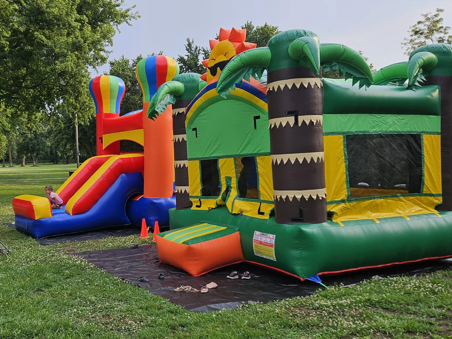 Tropical and balloon-themed bounce houses at an outdoor party